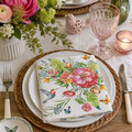 Hummingbird garden bouquet paper napkin folded on layered white plates with pink florals, a ceramic bird ornament and pink glassware on a springtime table setting
