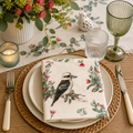 Kookaburra and gum blossom paper napkin folded on layered cream plates with a ceramic bird ornament, eucalyptus greenery and green glassware on a native-themed table setting