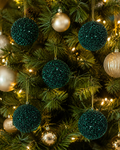 Dark green sequin baubles hanging on a Christmas tree among gold ornaments and warm fairy lights, close-up of sparkly texture