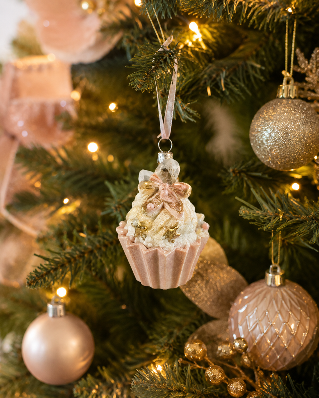 Gingerbread man cupcake ornament hanging on a Christmas tree branch among pink and gold baubles and ribbon