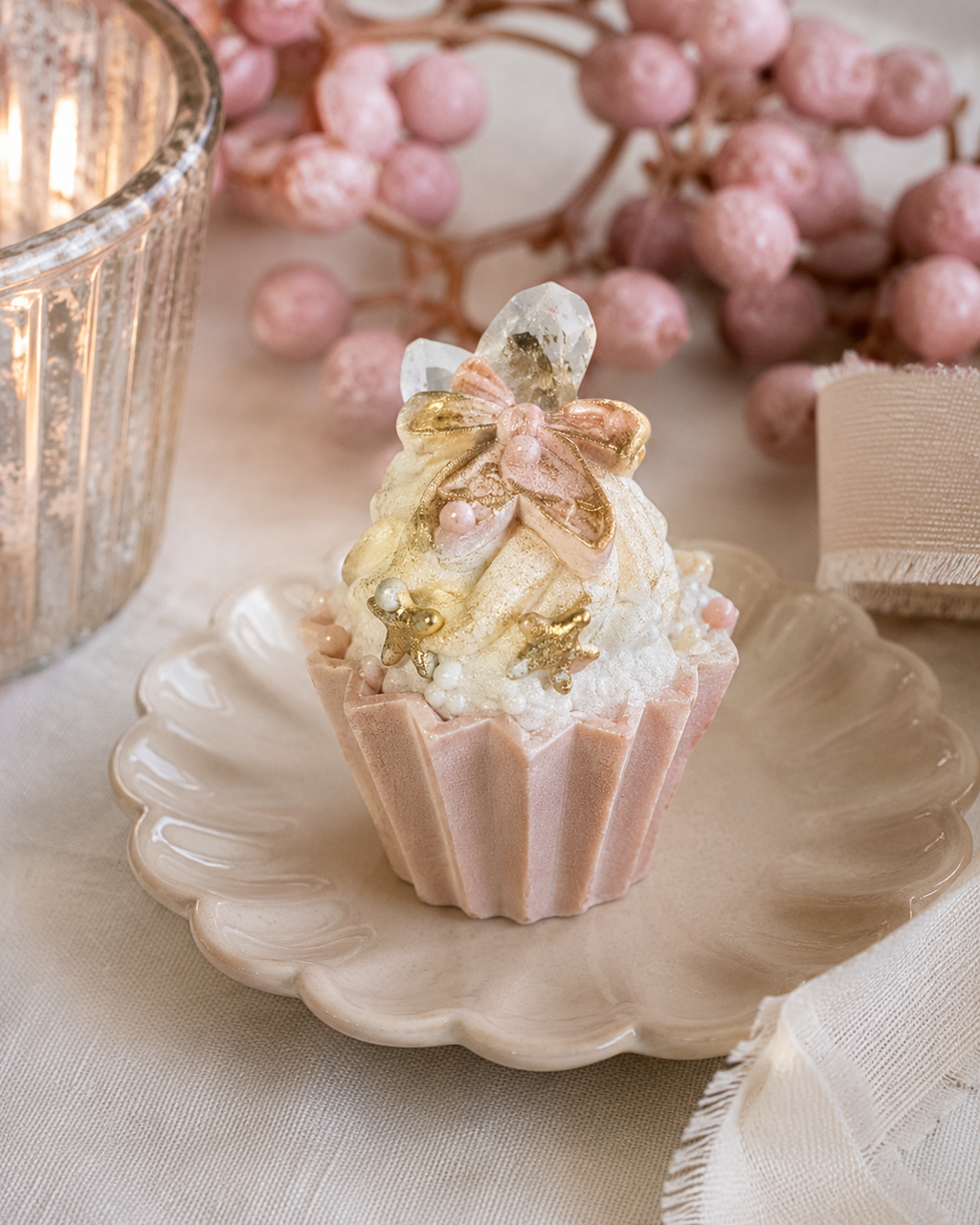 Gingerbread man cupcake ornament displayed on a cream scalloped plate beside a candle and pink berry sprigs