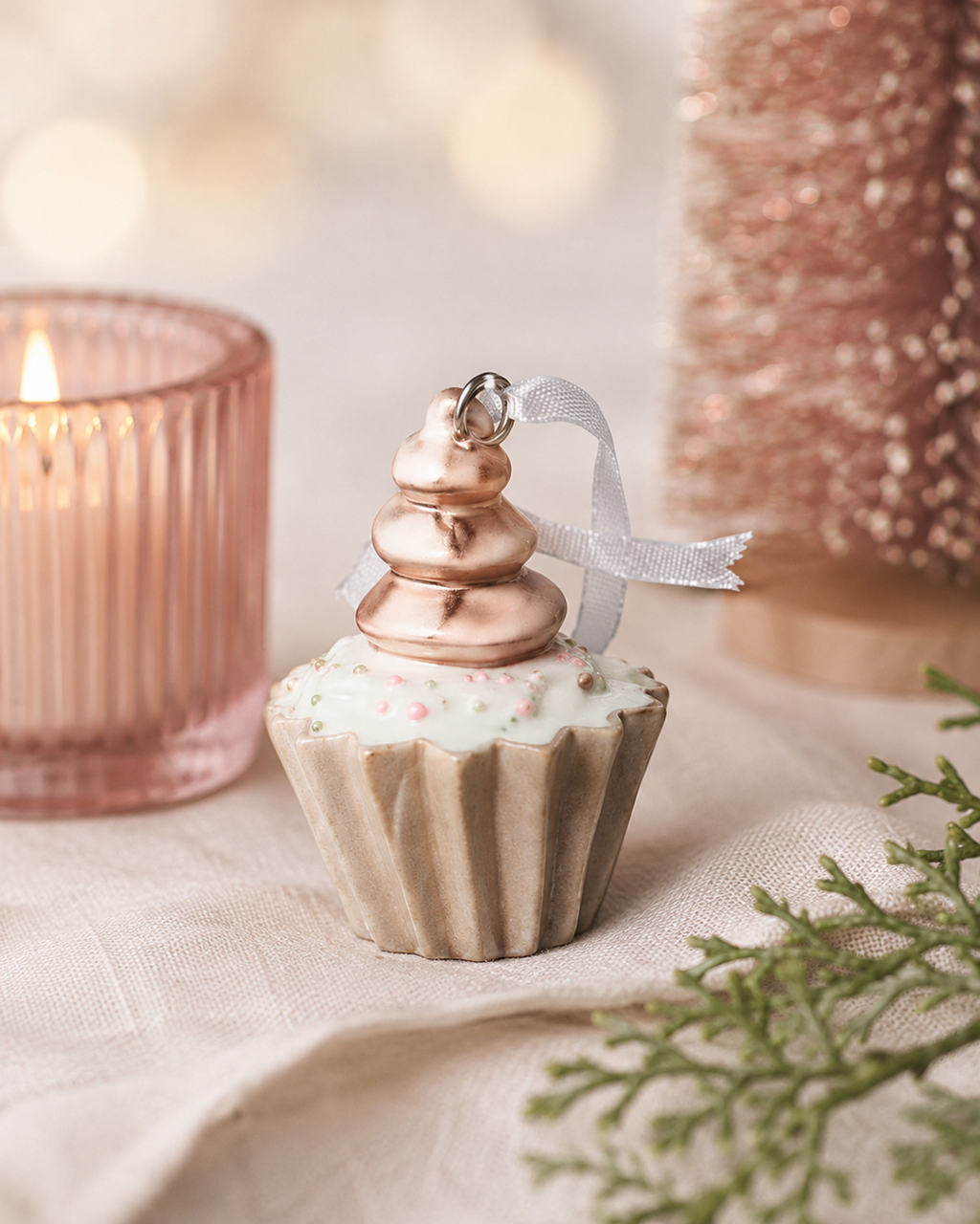 Pink swirl cupcake ornament displayed on a table beside a pink candle and a rose gold bottle brush tree