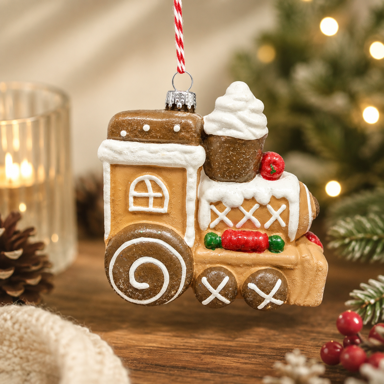 Gingerbread Train Hanging Ornament suspended against a warm styled background with candle, pine cones, and red berries