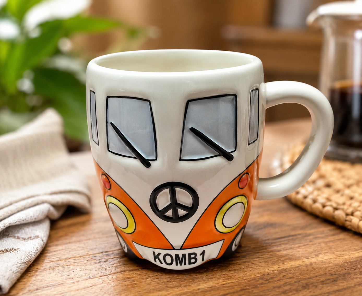 Orange Kombi van ceramic mug styled on a wooden table with a plant and french press in a cosy home setting, KOMB1 number plate visible
