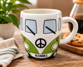 Green Kombi van ceramic mug filled with coffee, styled on a wooden table with a plant, candle and books in a cosy home setting