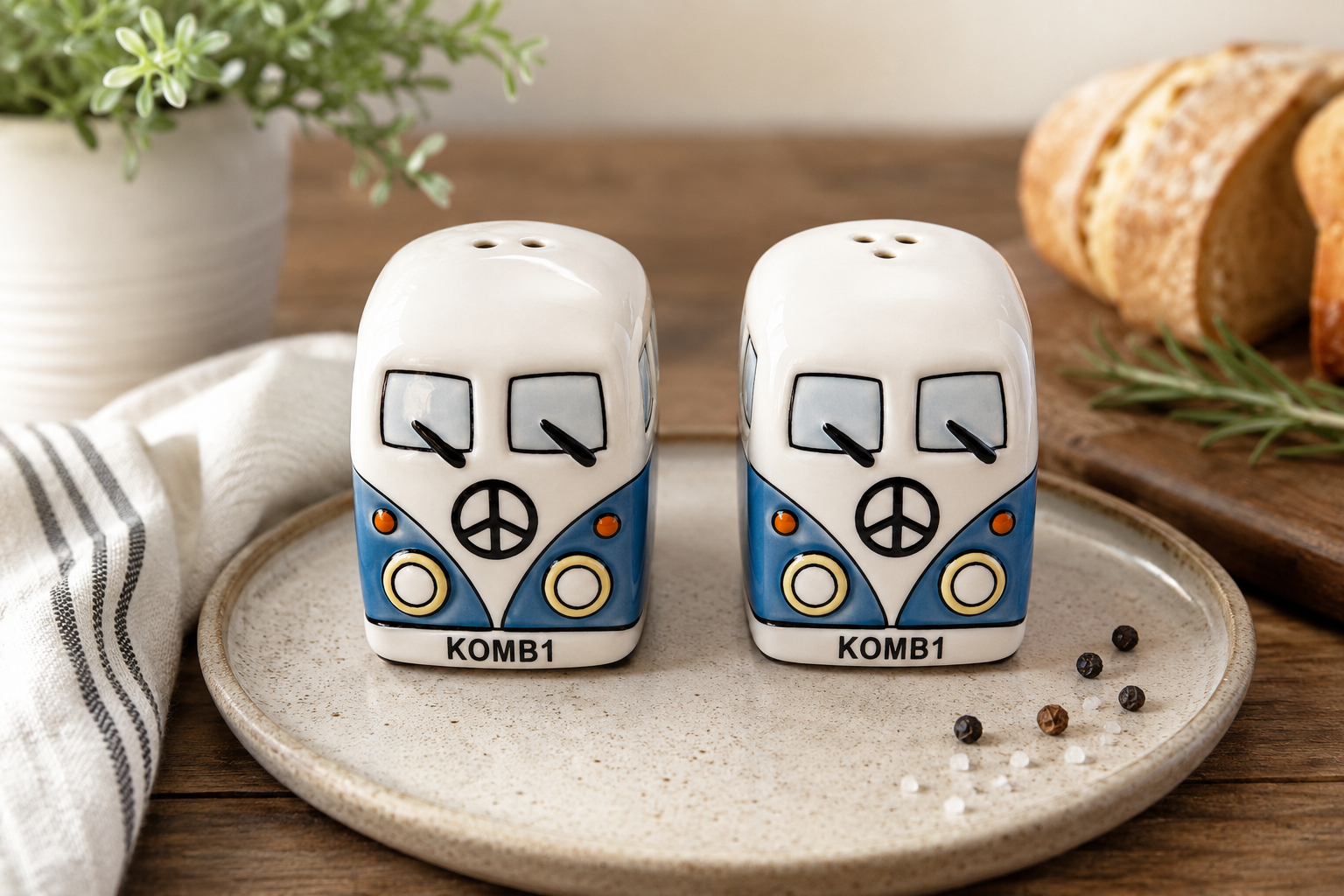 Kombi ceramic salt and pepper shaker set in blue and white, sitting on a cream speckled plate on a wooden table styled with bread, rosemary, and a striped linen
