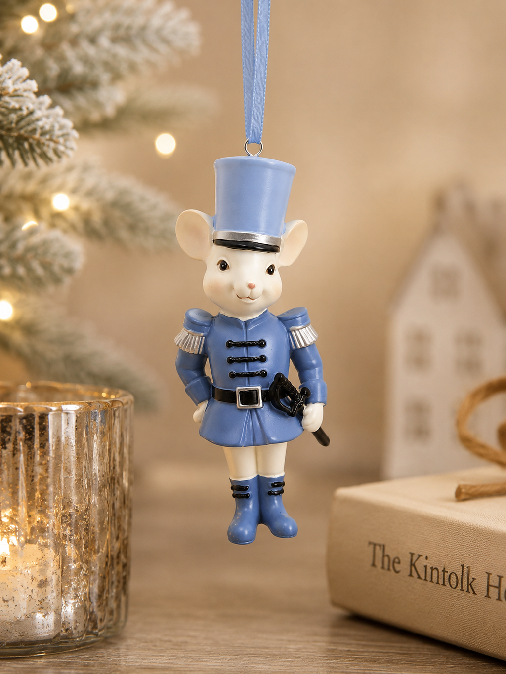 Blue mouse soldier Christmas tree ornament hanging from a frosted Christmas tree, styled with mercury glass candle holders and a white ceramic house, wearing a military uniform with silver epaulettes and top hat
