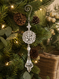 Silver crystal snowflake and drop Christmas ornament hanging on a lit Christmas tree with pine cones and eucalyptus, showing the decorative scroll hook, large snowflake medallion and faceted drop pendant