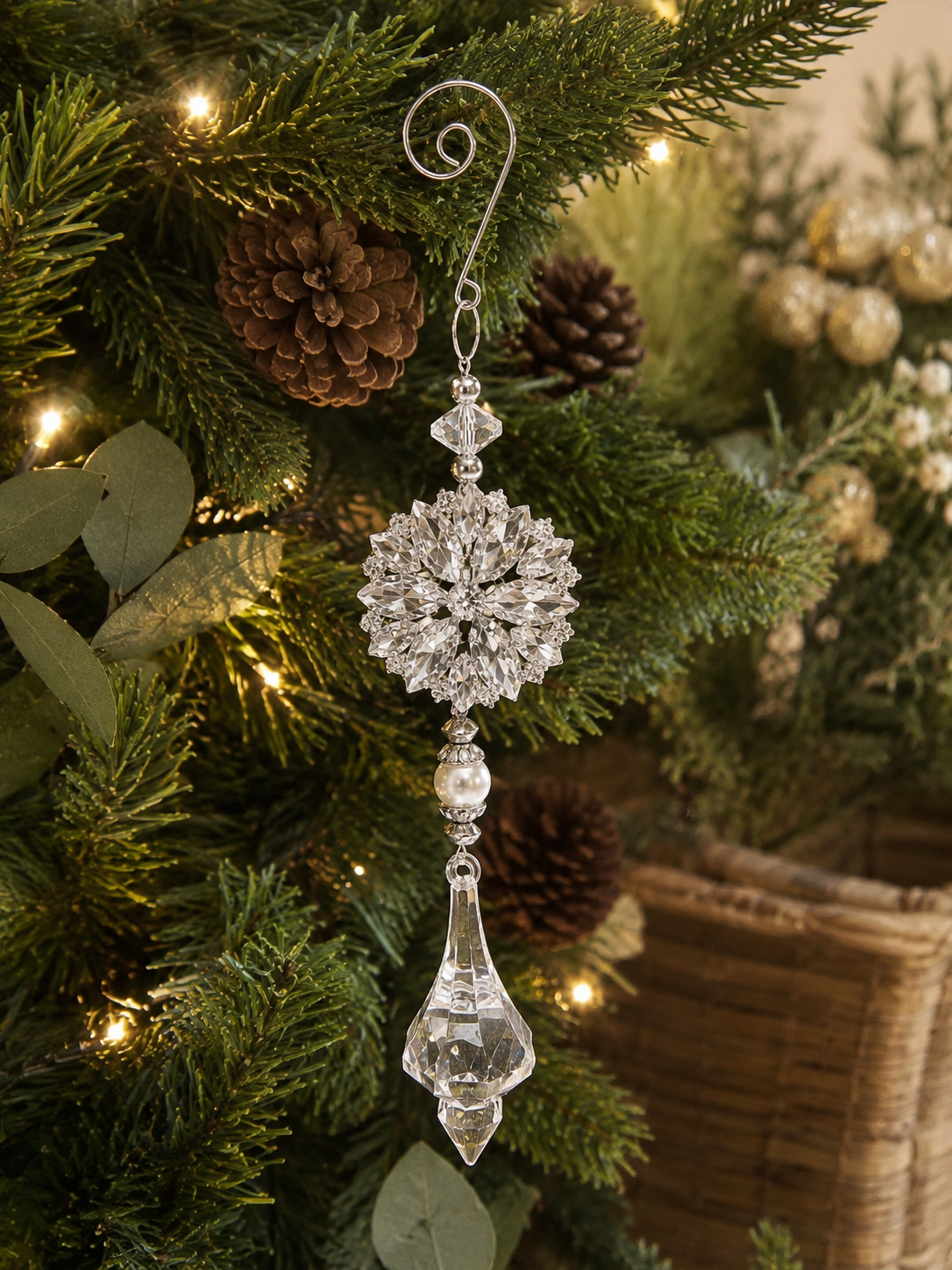 Silver crystal snowflake and drop Christmas ornament hanging on a lit Christmas tree with pine cones and eucalyptus, showing the decorative scroll hook, large snowflake medallion and faceted drop pendant