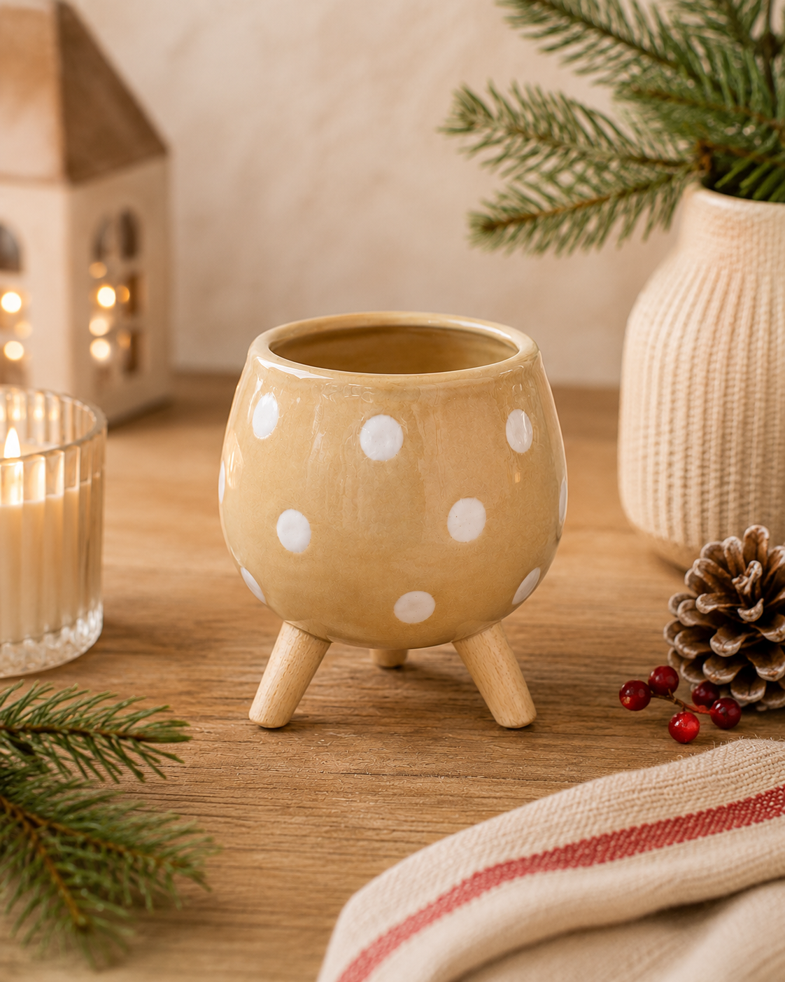 Mustard ceramic footed pot with unglazed spot detail styled on a timber surface with pine branches, candles, and a pinecone