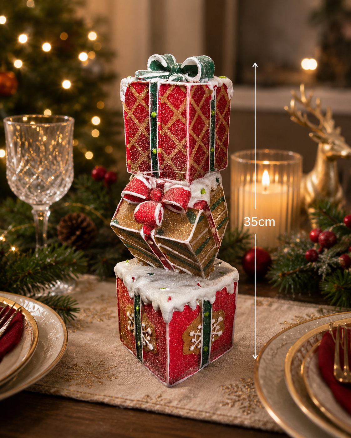 Glittery stacked gift box Christmas decoration used as a dining table centrepiece styled with crystal wine glasses, gold-rimmed plates, red napkins and a pine and red berry garland with fairy lights — 35cm high — Mistletoe Home