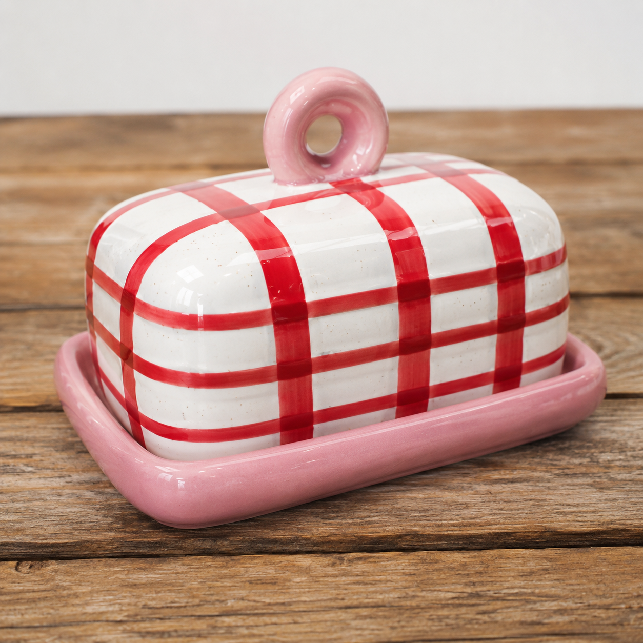 Red and white gingham ceramic butter dish with blush pink tray and ring handle on rustic timber surface