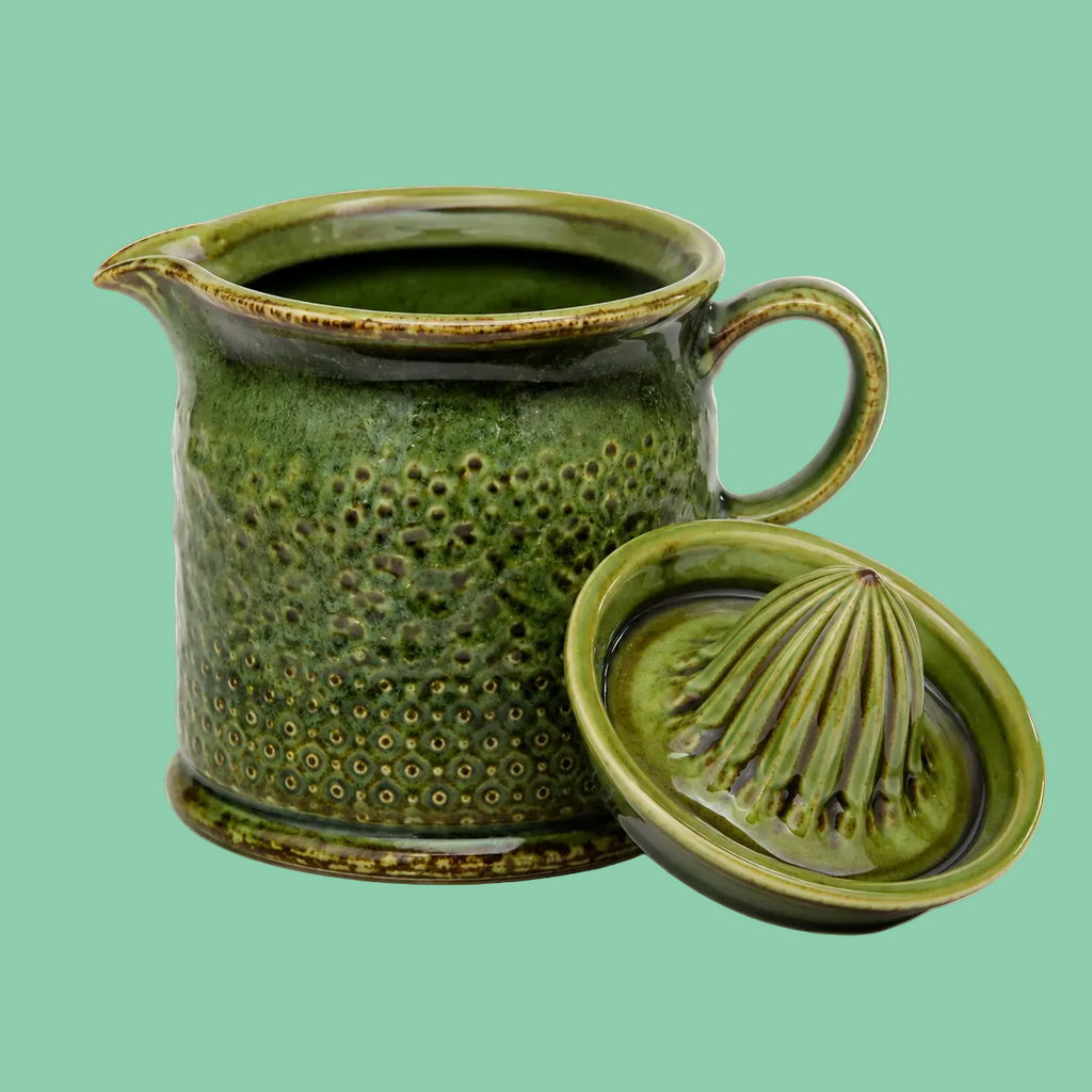 Green reactive glaze ceramic citrus juicer cone resting against spouted jug on mint green background, showing textured dimpled surface