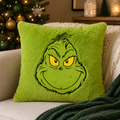 Grinch plush cushion sitting on a cream sofa next to a lit Christmas tree with gold and green ornaments