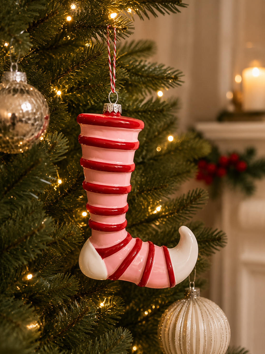 Pink and red candy stripe elf shoe Christmas ornament hanging on decorated tree — glossy curled toe elf boot with candy cane twist cord