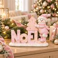Pink snowman NOEL resin Christmas sign styled on a timber sideboard, with frosted pine garland, fairy lights, a pink ribbon and a pastel Christmas tree glowing in the background