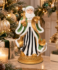 Green and gold Santa Claus figurine displayed on a marble console table beside a decorated Christmas tree, gold and green ornaments, and a lit candle