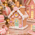 Pastel gingerbread house figurine with a gingerbread man, candy roof details, and glowing heart window, displayed on a marble table beside a Christmas tree and matching gingerbread houses