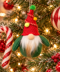 Plush gnome hanging ornament with red knitted hat, gold cord and pompoms, hanging on a Christmas tree beside a candy cane