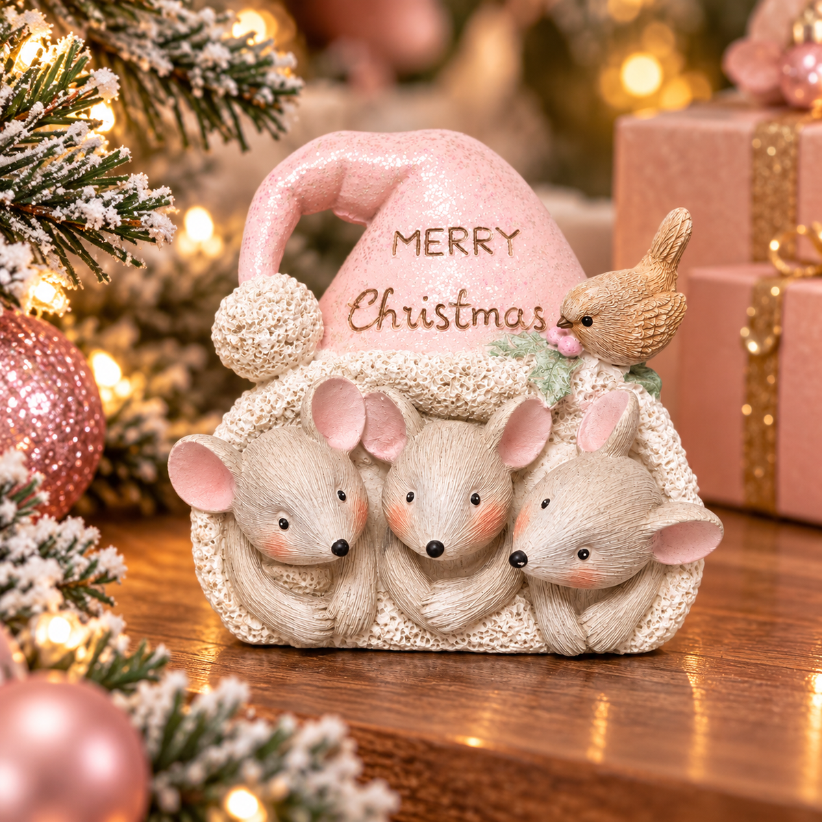 Three mouse faces peeking out from under a glittery pink santa hat with "Merry Christmas" lettering and a small bird on the brim, styled with pink Christmas decor