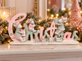 Pastel pink and sage "Christmas" word sign with mouse figurines and toy train styled on a mantel with candles and a glitter Christmas tree