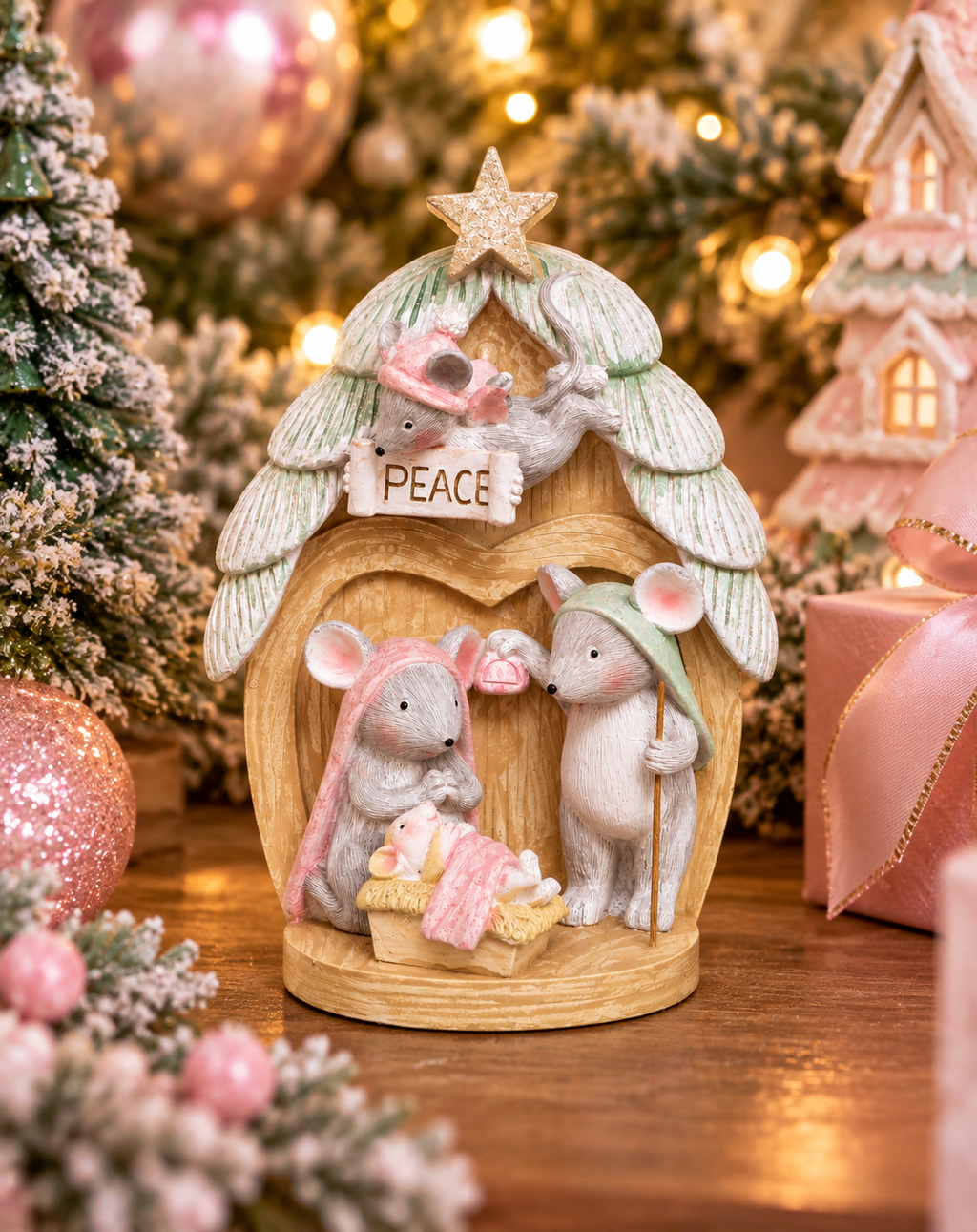 Pastel pink and green mouse nativity scene figurine with angel mouse holding a peace banner, styled among pink Christmas trees and gifts