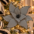 Black and white striped poinsettia flower stem with glitter-edged petals nestled in a black and gold monochrome Christmas tree, striped ribbon and warm fairy lights in the background