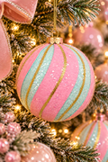 Pink and mint glitter bauble with gold swirl stripes hanging on a pastel Christmas tree, pink velvet bow and warm fairy lights in the background