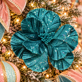 Deep teal glitter magnolia flower stem nestled in a pastel pink and mint Christmas tree, surrounded by velvet bows and warm fairy lights