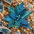 Teal velvet poinsettia flower stem with glitter-dusted tips nestled in a jewel-toned Christmas tree, teal velvet bow and warm fairy lights in the background