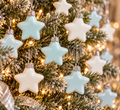 Duck egg blue and white glass star ornaments hanging on a flocked Christmas tree with silver ribbon and warm fairy lights