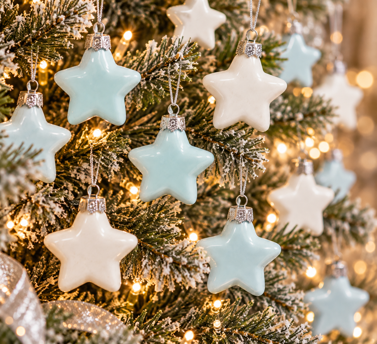 Duck egg blue and white glass star ornaments hanging on a flocked Christmas tree with silver ribbon and warm fairy lights
