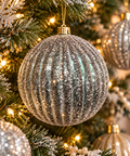 Silver glitter ribbed Christmas bauble hanging on a decorated tree, close up showing fluted texture and green undertones with fairy lights and other gold ornaments in the background