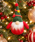 Small red and green gnome hanging ornament on a Christmas tree branch, surrounded by red berries, fairy lights and gold baubles