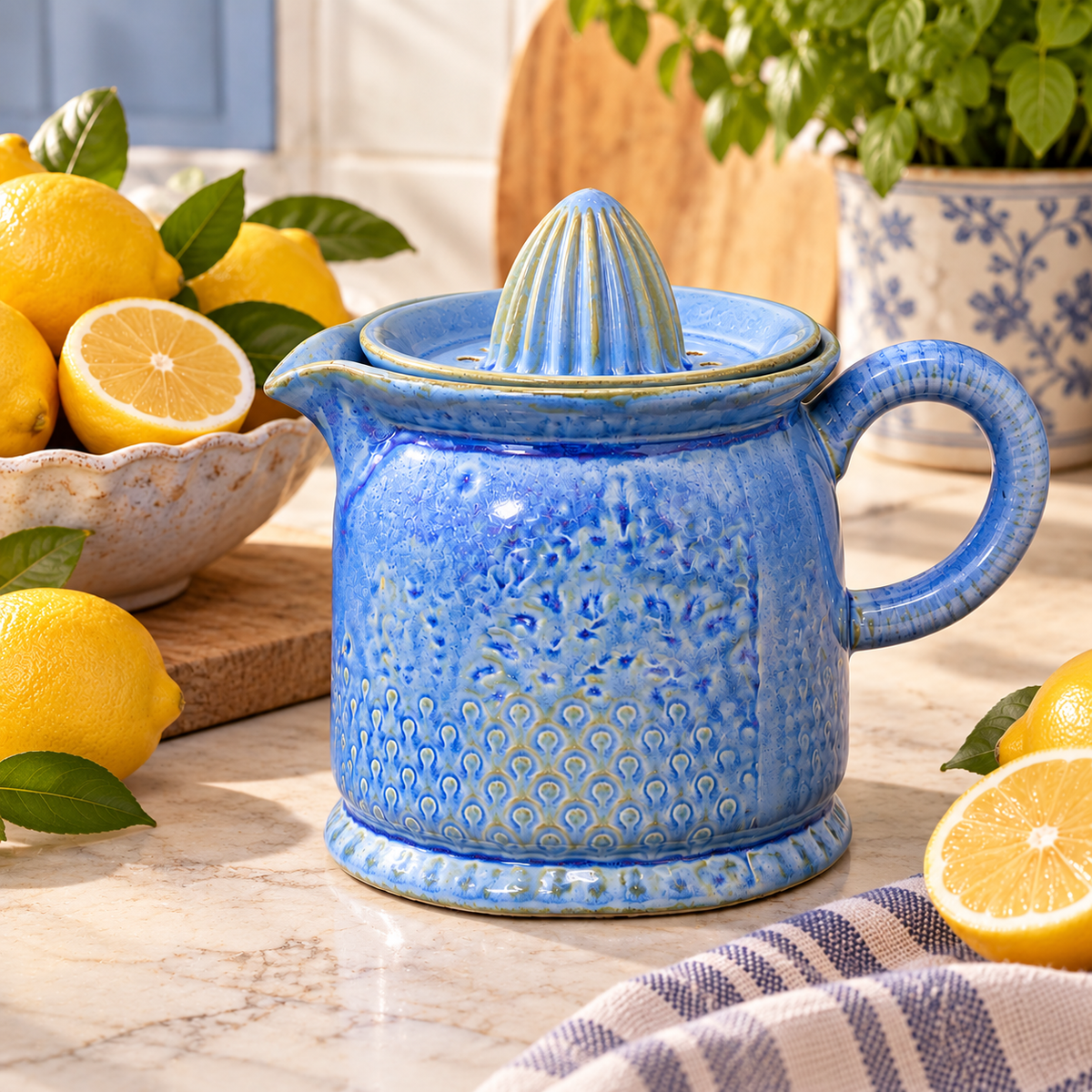 Blue reactive glaze ceramic citrus juicer assembled on a marble benchtop, styled with fresh lemons, a blue floral planter and a striped tea towel