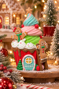 Cupcake-shaped gingerbread house decor with gingerbread people figures, styled on a wooden stand beside a gingerbread village, snowy mini trees and red baubles