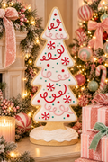 Peppermint gingerbread Christmas tree decor styled on a mantel beside a lit candle and pink glitter bows, with a decorated Christmas tree and wrapped gifts in the background