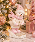 Pink and cream skiing snowman figurine with a pearl-beaded hat, pink scarf and gold skis, styled beside a snowy Christmas tree, pink baubles and a velvet bow