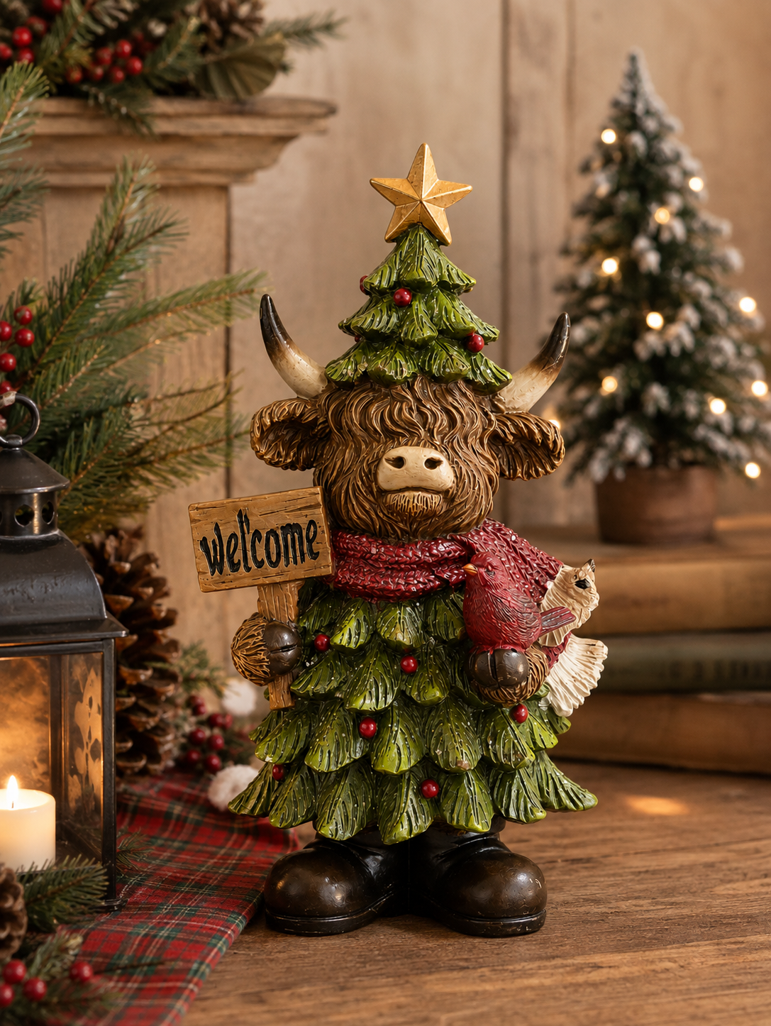Highland cow Christmas figurine dressed as a pine tree, holding a wooden Welcome sign with a red cardinal perched on its other hand, displayed near a lantern and pine garland with a snowy mini Christmas tree in the background