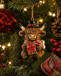 Highland cow Christmas ornament wearing a black top hat and holding a wrapped gift, hanging on a Christmas tree branch next to a red bauble and pinecone