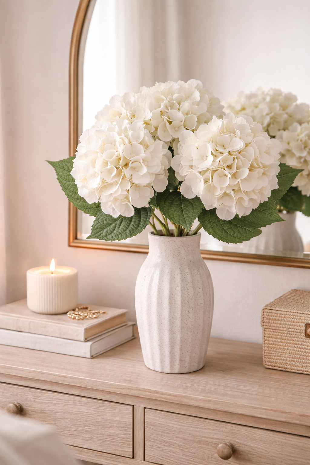 White faux hydrangea stems styled in a speckled ceramic vase on a timber dresser with gold mirror candle and books — Hamptons home décor Australia Mistletoe Home