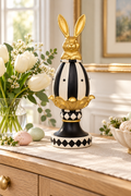 Gold bunny figurine on a black and white striped egg with gold petal collar and harlequin pedestal, styled on a timber sideboard with white tulips and speckled pastel Easter eggs