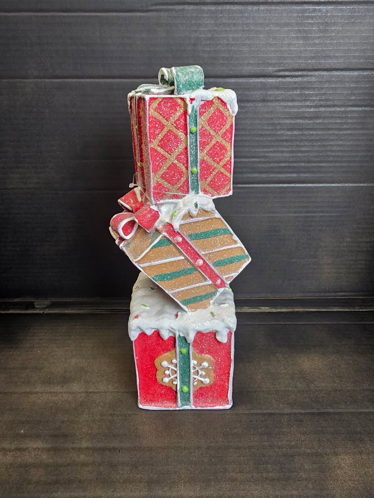 Three-tier stacked Christmas gift box decoration in red, gold and green with glitter finish, snow drips, gingerbread motifs and ribbon bows on dark background — Mistletoe Home