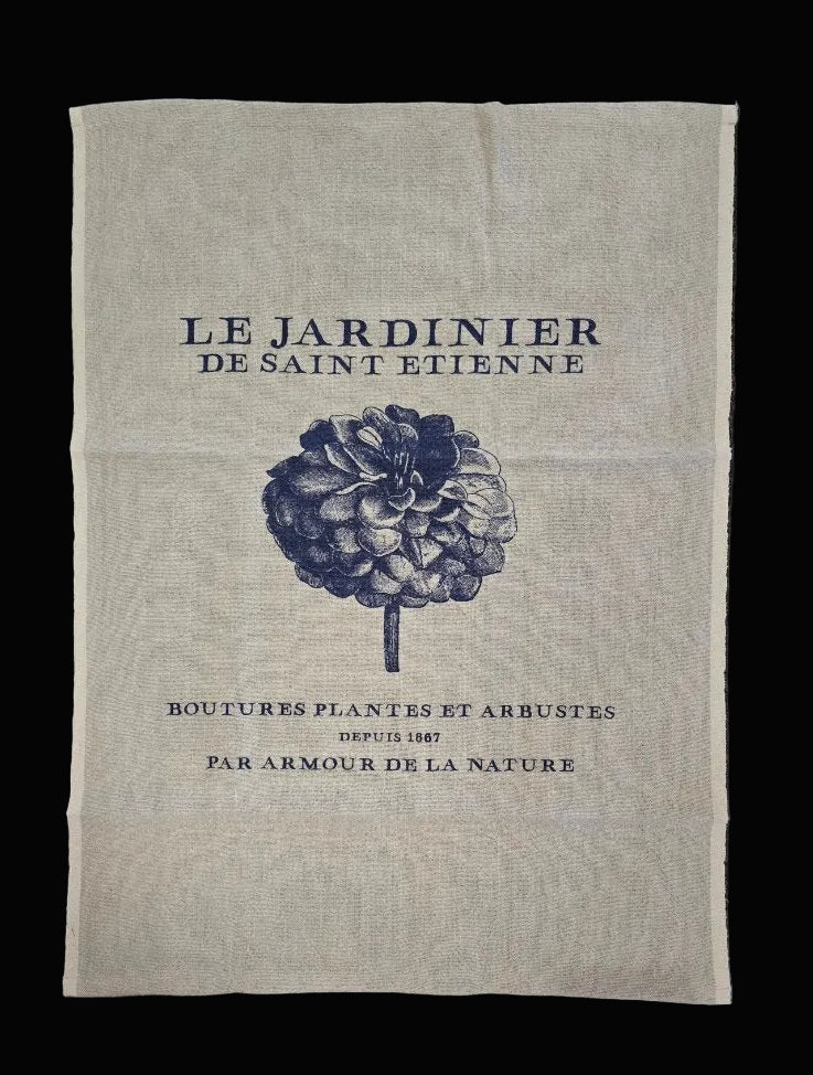 Flat lay of natural oatmeal linen tea towel showing full Le Jardinier de Saint Etienne navy botanical print with dahlia illustration and French typography on black background — Mistletoe Home