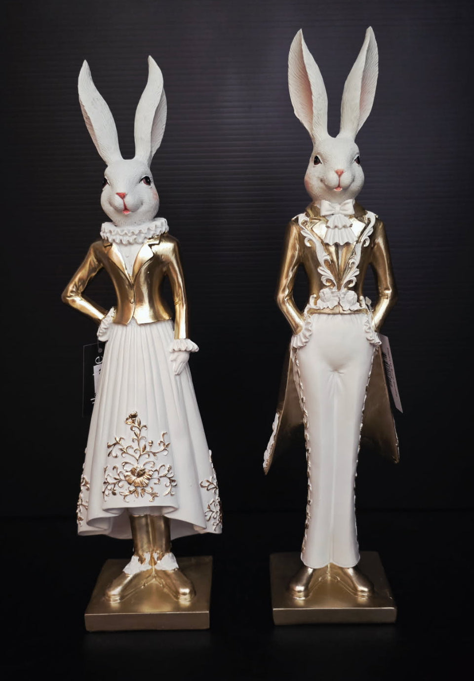 Two rabbit statues in formal attire on a black background