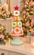Pastel donut Christmas tree decoration with red star topper on a pink and mint pedestal stand, styled on a white sideboard with a blush Christmas tree, baubles, fairy lights and a wrapped gift