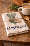 La Betterave linen tea towel folded and tied with natural twine bow and 100% linen tag, styled on a rustic timber table with coffee cup, wooden spoon and fresh thyme — Mistletoe Home