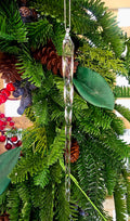Clear glass twisted icicle Christmas ornament hanging on a green Christmas tree decorated with pine cones, red berries and magnolia leaves, showing the spiral form and tapered point