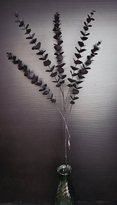 artificial eucalyptus branch in a green vase against a dark textured background