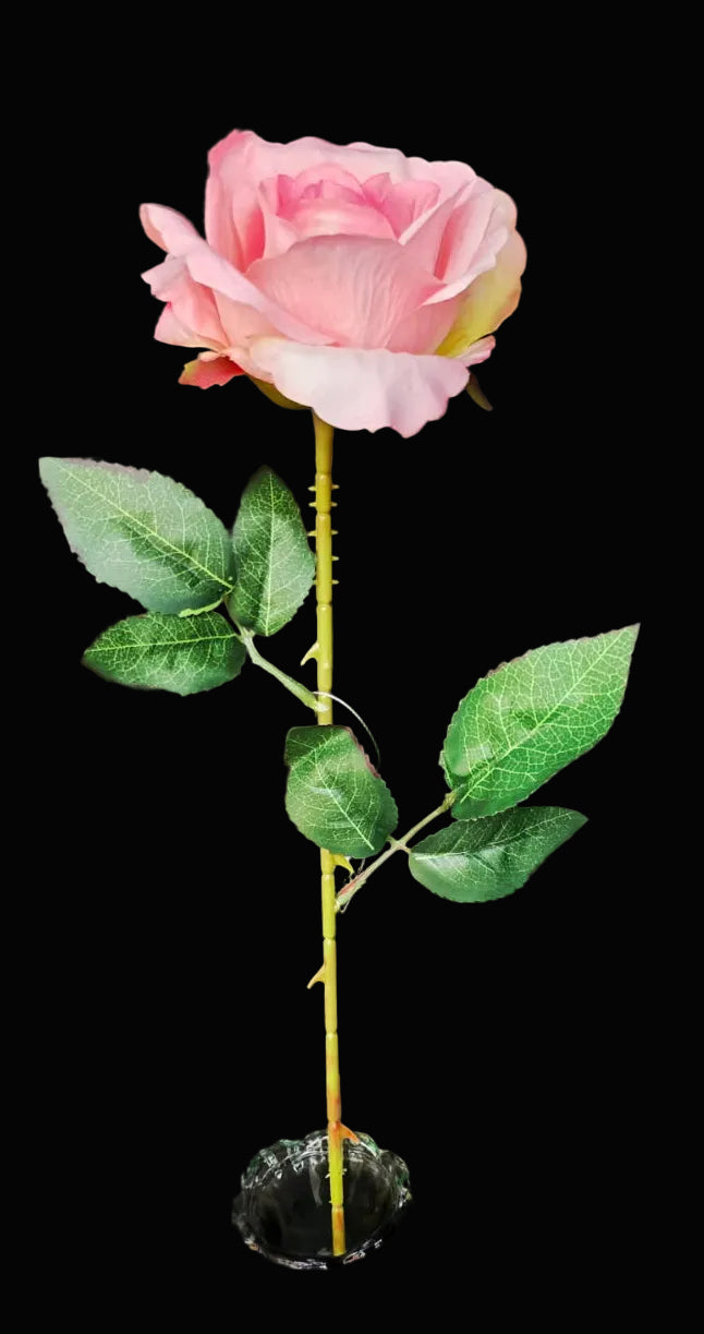 Pink artificial rose in a green vase on a dark surface
